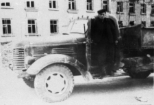 Mężczyzna przy ciężarówce, w tle budynek.