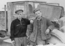 Dwóch mężczyzn w strojach roboczych na tle ciężarówki.