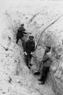 Mężczyźni w strojach roboczych kopiący rów.