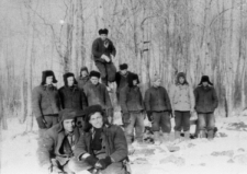 Grupa mężczyzn w kufajkach i uszankach w lesie.