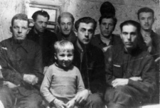 Więźniowie zwolnieni z łagrów. Grupa mężczyzn we wnętrzu, z przodu kilkuletnie dziecko. Od lewej: NN, Stanisław Kupraszewicz, Józef Nowicki, NN, NN, Ilkiewicz, NN. Fotografia wykonana w 1955 lub 1956 roku.