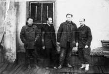 Więźniowie zwolnieni z łagr&oacute;w. Czterech mężczyzn na tle budynku. Od lewej: Stanisław Kupraszewicz, Piotr Adaś, Władysław Szarko, J&oacute;zef Krypajcis. Fotografia wykonana w 1955 lub 1956 roku.