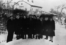 Grupa mężczyzn i kobiet w zimowych ubraniach na tle zabudowań.