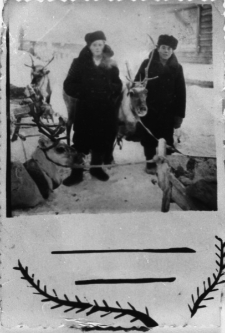Dwóch mężczyzn w płaszczach i futrzanych czapkach obok zaprzęgu reniferów.