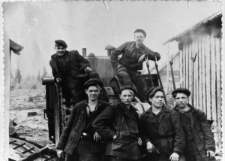 Sześciu mężczyzn w strojach roboczych upozowanych na dużej maszynie.