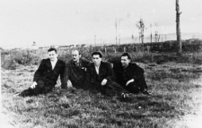 Polacy, byli więźniowie łagru D-2. Czterech mężczyzn siedzi na tle letniego krajobrazu. Pierwszy z lewej: Jerzy Różanowski. Pozostałe osoby nierozpoznane. W tle obóz D-2.