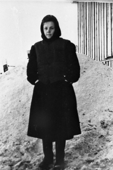 Zuzanna Raubo, więźniarka łagrów (kobieta w zimowym ubraniu na tle drewnianego domu). Fotografia prawdopodobnie z 1955 roku.