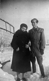 Mężczyzna i kobieta w strojach zimowych, stoją przy metalowym ogrodzeniu.
