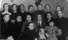 Grupa osób we wnętrzu, w pierwszym szeregu mężczyzna ze szczeniakiem.