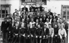 Grupa osób pod transparentem pozdrawiającym przodowników pracy; czwarty od lewej siedzi: Bałakir (major, naczelnik obozu).