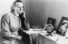 Maria Ostrołuch. W Kingirze po pacyfikacji. Kobieta siedząca przy stoliku, przed nią fotografie i budzik.