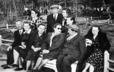 Grupa ludzi siedzących na ławce. W tle zagajnik. Siedzą od lewej: NN, Krystyna Zajączkowska-Rudnicka, Alina Kopisto, Nela Mackiewicz, Andrzej Mackiewicz, Janina Durlik. Osoby w górnym rzędzie nierozpoznane.