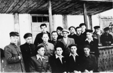 Grupa zesłańców przed drewnianym budynkiem.