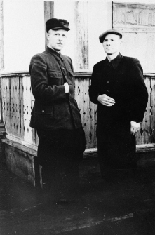 Dwóch mężczyzn przed drewnianym budynkiem.