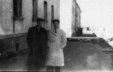 Dwóch mężczyzn na ulicy, obok murowanego budynku. Pierwszy z lewej w płaszczu: Czesław Jakimowicz. Zdjęcie z 1956 lub 1957 roku.