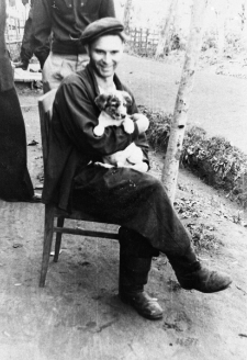 Wojciech Zakrzewski, siedzący na krześle ze szczeniakiem na kolanach.