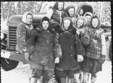 Grupa kobiet w waciakach i chustkach przy ciężarówce.