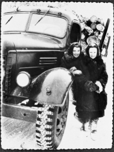 Dwie kobiety przy ciężarówce załadowanej drewnem.