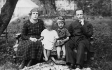 Kobieta, mężczyzna i dwoje dzieci, siedzący na ławce w ogrodzie.