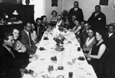 Grupa osób siedzi za zastawionym stołem.