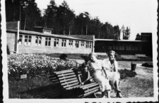 Dwie kobiety i dziecko na ławce przed parterowymi budynkami.