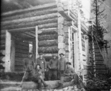 Brygada ciesielska złożona z przymusowo osiedlonych, zwolnionych z łagrów. Grupa mężczyzn w strojach roboczych przy nie skończonym budynku z drewnianych bali.