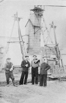 Czterech mężczyzn w strojach roboczych na tle wyciągu kopalni.