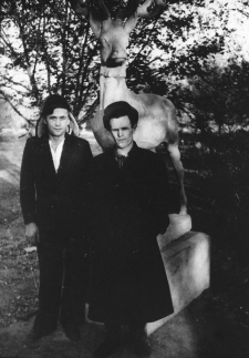 Dw&oacute;ch mężczyzn więźni&oacute;w łagru na tle drzew i figury sarenki (?).