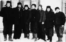 Grupa mężczyzn w strojach roboczych na tle budynku. Trzeci od prawej: Stanisław Kowalewski po zwolnieniu z łagru, pozostałe osoby NN; zdjęcie z 1955-56 roku.