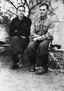 Dw&oacute;ch mężczyzn siedzących na murku pod drzewem.