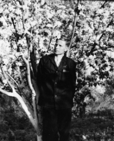 Medard NN w obozowym gospodarstwie. Mężczyzna pod drzewem owocowym. Podpis na odwrocie: "Rodaczce - pani Kazi na pamiątkę przyjaźni spędzonych dni na obczyźnie w obozie pracy niewolniczej, Medard".