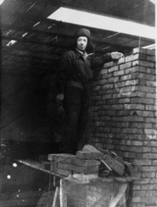 Józef Gryguś w łagrze (?). Mężczyzna w stroju roboczym na rusztowaniu, przy murze z cegieł.