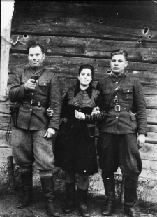 Kobieta z dwoma mężczyznami w mundurach na tle ściany z drewnianych belek. Od lewej: Kazimierz Impierowicz "Olbrzym" (z pistoletem), Tekla Impierowicz (obecnie Komar), NN; fotografia prawdopodobnie wykonana w latach 40-tych.