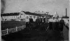 I Kapitalna. Grupa mężczyzn idzie drogą. W tle budynki.