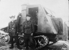 Dwaj mężczyźni w czapkach-uszankach przy pojeździe na gąsiennicach.