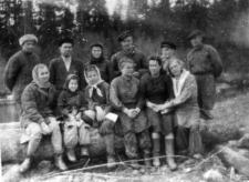 Kilka kobiet w roboczych ubraniach siedzi na pniu zwalonego drzewa, za nimi stoi pięciu mężczyzn i kobieta; podpis na odwrocie: "Bułtusuk pracownicy "kantory" i majstrowie 1949 rok".