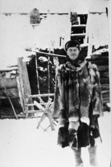 Mężczyzna w ubraniu z kawałków futra przed rozwalającym się drewnianym domem. Bolesław Stankunowicz z Bukańców pow. Wiłkomierz, Litwa Kowieńska. Wywieziony w 1941 roku na Syberię - przed własnym domem.
