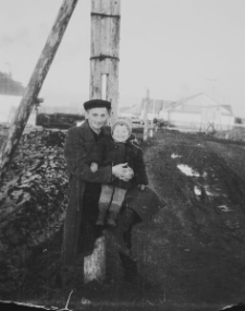 Mężczyzna z dzieckiem, w tle baraki dawnego łagru.