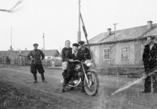 Chłopak na motocyklu, w tle baraki dawnego obozu, z prawej stoi Bernard Grzywacz.