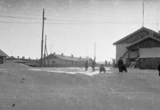 Dzieci zjeżdżające na sankach, w tle baraki dawnego łagru.