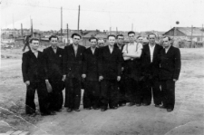 Polacy po zwolnieniu z łagru, drugi od lewej stoi Jan Marcinkiewicz, pierwszy od prawej Stanisław Romaszko, czwarty z prawej Antoni Marcinkiewicz. W tle łagier (prawdopodobnie nr 2) przerobiony na hotel dla więźniów wychodzących na wolność.