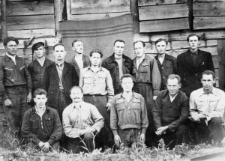 Więźniowie łagru Nowoczunka przy trasie Tajszet-Brack. Stoją od prawej: J&oacute;zef Hałyna (żołnierz AK z okolic Dyneburga), Bronisław Wieliczko (nowogr&oacute;dzka AK), Henryk Stawryłło (AK Litwa Kowieńska), Henryk Kuczyński (nowogr&oacute;dzka AK), Zenon Bielski (grodzieńska AK), Sergiusz (nazwisko nieznane, z Wilna), NN, Kazimierz Tarnawski (wołynianin, żołnierz Andersa, aresztowany po powrocie do Polski), Adamowicz (nowogr&oacute;dzka AK); siedzą od prawej: Bronisław Możdżer (z LWP do łagru), J&oacute;zef Legun (nowogr&oacute;dzka AK, LWP i łagier), Franciszek (nazwisko nieznane, nowogr&oacute;dzka AK), Bubnowski (z Sopoćkiń, nowogr&oacute;dzka AK), Bolesław Jackiewicz (z Sopoćkiń, nowogr&oacute;dzka AK). W tle suszarnia cegieł, w obozie produkowano materiały budowlane do budowy brackiej elektrowni.