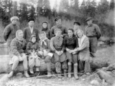Kilka kobiet w roboczych ubraniach siedzi na pniu zwalonego drzewa, za nimi stoi pięciu mężczyzn i kobieta; podpis na odwrocie: "Bułtusuk pracownicy "kantory" i majstrowie, 1949 rok".