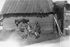 Rodzina polska na zesłaniu. Rodzice w waciakach i dziecko z lalką - Elwira Adamczewska z matką i ojcem. Za nimi szopka-domek wybudowany przez ojca nad rzeką Tom. Podpis na odwrocie: "Rodzina Szpyncowiczów [?] podczas wygnania w Syberyji w 1940-46 r."