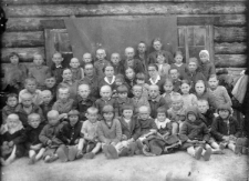 Uczniowie i nauczyciele szkółki polskiej zorganizowanej w zamieszkałym przez większą grupę depotowanych Polaków "posiołku", zwanym - 98 kilometr. W środku siedzą: pan Potocki - przedstawiciel Związku Patriotów Polskich; w białym kołnierzyku z dzieckiem na kolanach nauczycielka p. Elżbieta Czyżewska; druga kobieta w białym kołnierzyku, również nauczycielka p. Leokadia Szlachciuk; pomiędzy nimi pani przygotowująca posiłki dla dzieci; pierwsza z prawej, w białej chustce siostra Ireny Bejnarowicz - Marta.