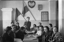 Nauczyciele z polskiej szkoły w pokoju nauczycielskim. Od lewej: Goldman (była nauczycielka szkoły powszechnej w Polsce), NN (nauczyciel gimnastyki), Maria Brysk-Rajsfeld (mgr psychologii, uczyła języka polskiego), NN (inżynier, uczył fizyki i chemii); z tyłu od lewej: Goldblatt (uczył angielskiego), Alicja Szenberg-Maliniak (studentka UJ, uczyła w młodszych klasach), Jakub Gises (stoi; dyrektor szkoły, przedwojenny nauczyciel w szkole powszechnej), mgr Tabacznik (matematyczka), NN. Po prawej stronie stołu siedzą od prawej: NN (Rosjanka, uczyła rosyjskiego), mgr Tatiana Bernstain (historyk, nauczycielka historii). Z tyłu od prawej: Danuta Barzach (psycholog, nauczycielka polskiego w klasach V-VI), pozostali NN.