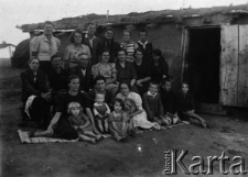 Grupa Polak&oacute;w przed lepianką. Z przodu na wercie siedzą obok małych dzieci: NN, NN, Wilhelmina Szuszkiewicz, Mietek Wierzba, Jędrek Wandurski i NN. Siedzą: NN, NN, NN, Ziszkowa, Leopoldyna Urbanowska, NN, Krysia Rogojska (?). Stoją: Maria Wierzba, Zofia Wandurska, Staszek Szuszkiewicz, Lucia Śliwińska, Śliwińska, Artur Śliwiński. Zdjęcie wykonano "na lewo" przy okazji "paszportyzacji".