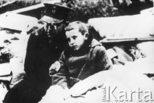 Chłopiec w palcie siedzi obok żołnierza.