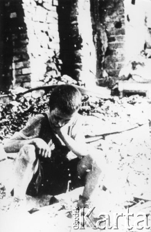 Chłopiec siedzący na gruzach domu.