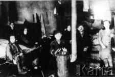 Kilka os&oacute;b siedzi w pomieszczeniu przy piecyku.